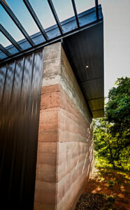 Exterior rammed earth wall with Metal siding wall and pergola.